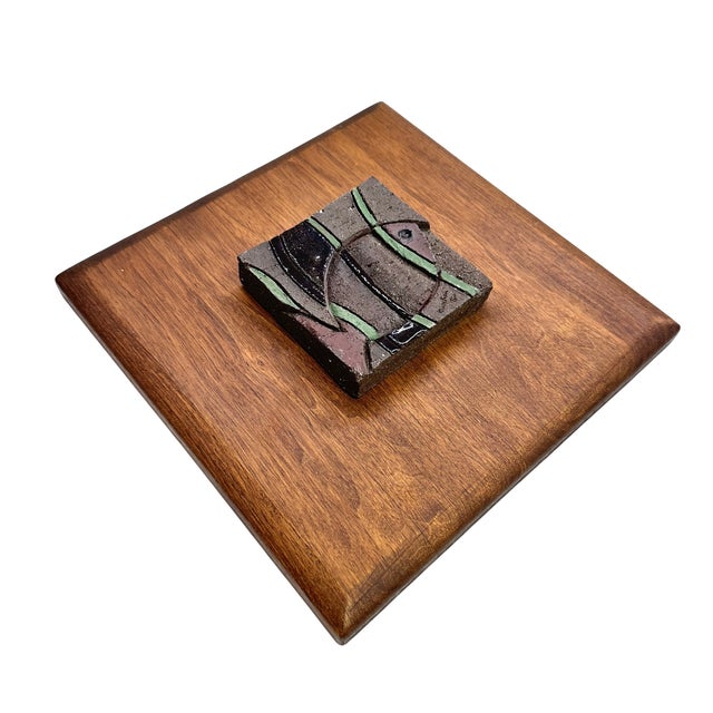 A distinctive vintage wall sculpture featuring an abstract ceramic fish relief mounted on a substantial wood panel. The...