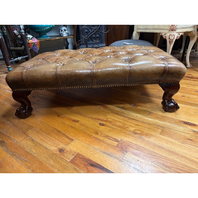 Antique Brown Leather tufted ottoman. Carved solid wood, ball and claw feet. Trimmed with antique brass nail heads....