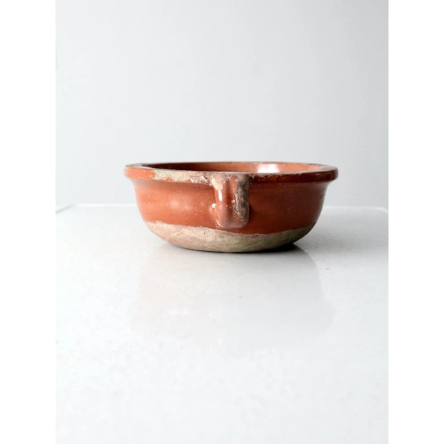 A low, handled earthenware bowl in a warm terracotta glaze with a gently timeworn rim that reflects years of use. simple,...