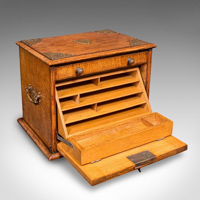 This is an antique stationery box. An English, golden oak and brass fall front desk tidy, dating to the Edwardian period,...
