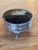 Round box raised on three small shaped feet, the glossy dark lid inlaid with a steamship under full flags, twin funnels...