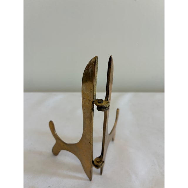 A vintage brass folding display easel with graceful curved feet and an adjustable center hinge. The warm patinated brass...