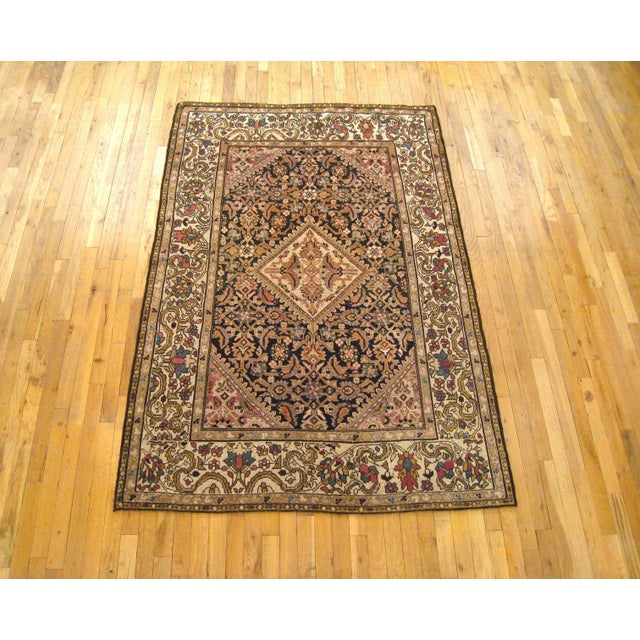 An antique Persian Malayer oriental rug, circa 1920. This fine hand-knotted wool rug features an ivory diamond-shaped...