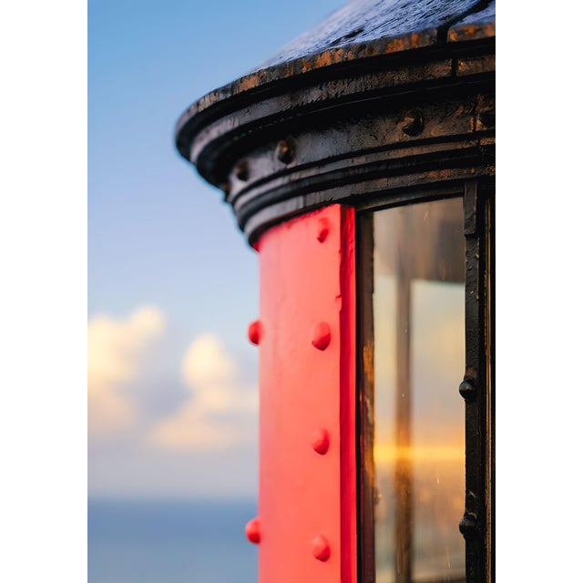 Coastal architectural artwork featuring a vivid red lighthouse exterior contrasted with the warm glow of a Fresnel lens,...