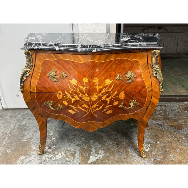 Design Plus Gallery presents a Louis XV Style French Bombe Commode. It has a black marble top, floral marquetry, and...