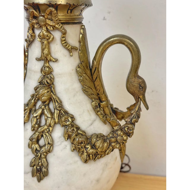 Pair of French Louis XVI Style White Marble & Gilt Bronze Swan-Handle Urn Lamps A grand pair of French Louis XVI-style...