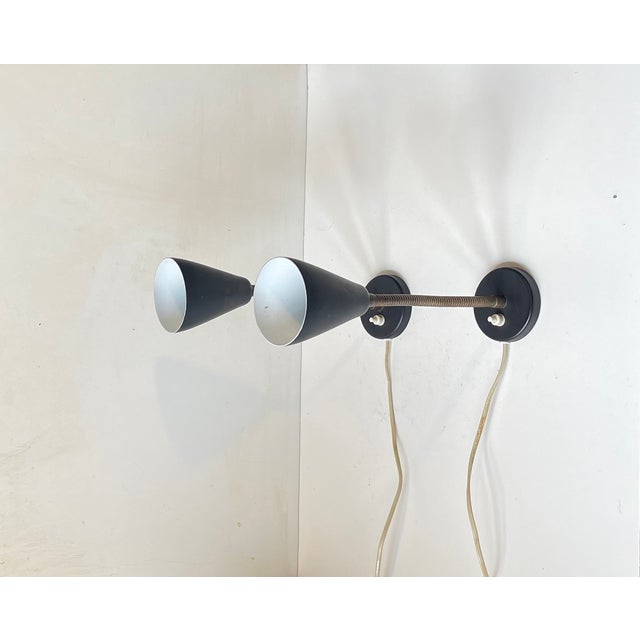 There is a vibe of Serge Mouille over these stylish satin black wall lights from German Raiss Leuchten. The shades and...