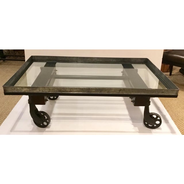 Stylish industrial modern cocktail table on wheels, metal frame and a glass top, showroom floor sample, original retail $1375