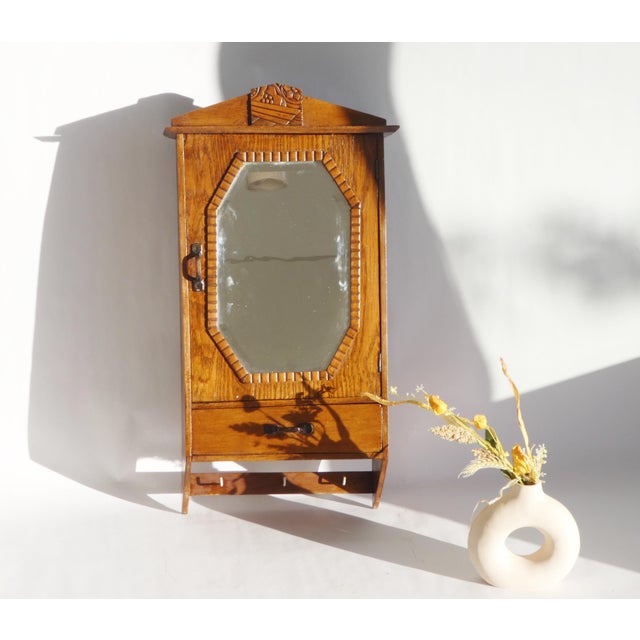 A beautiful Art Deco wooden wall cabinet with an octagonal shaped beveled mirror. It has a nice floral ornament on the top...