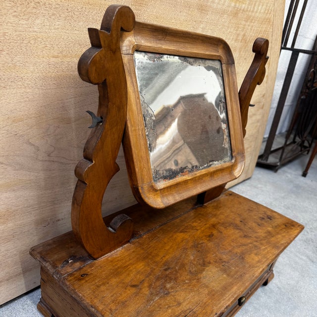Charming antique dressing mirror in solid wood, mounted on a small storage box with a drawer on the front. The mirror is...