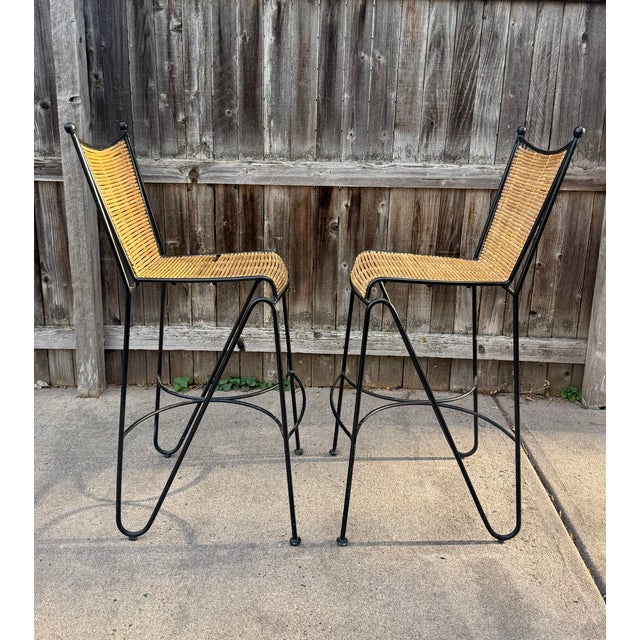 Striking pair of mid-century modern bar stools featuring sculptural black-finished wrought iron frames with distinctive...