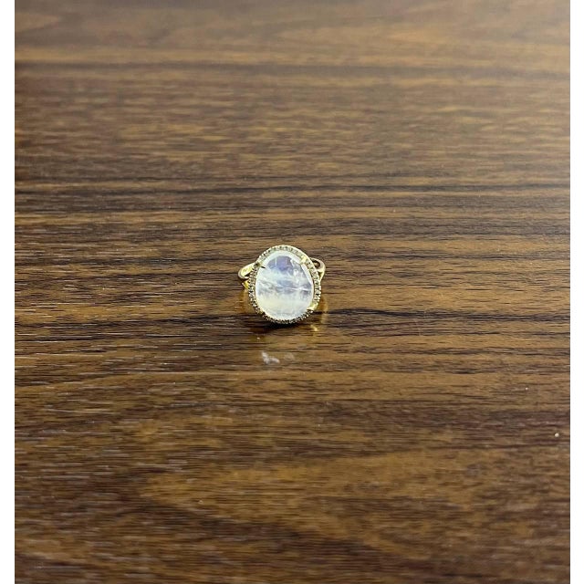 This exquisite ring features a captivating oval white moonstone, set in a 14k gold band. The gemstone is encircled by a...