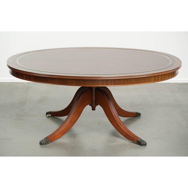 This elegant, oval, English-style coffee table features a red leather top and dates from the 20th century. This...