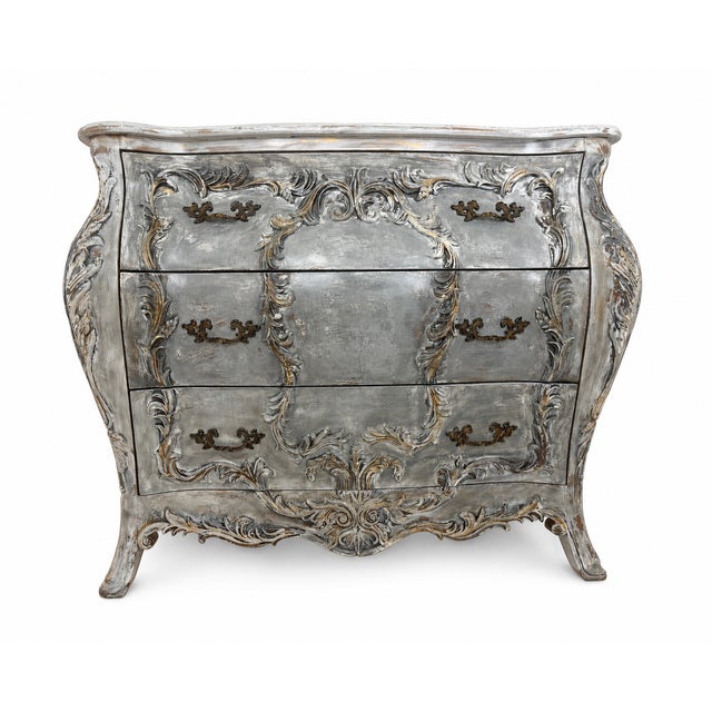 A stunning French Provincial bombé chest featuring elaborate carved floral and scroll work, finished in a distressed...