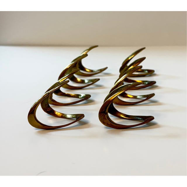 A distinctive set of eight vintage brass napkin rings featuring an elegant sculptural form. Each piece has a sweeping,...