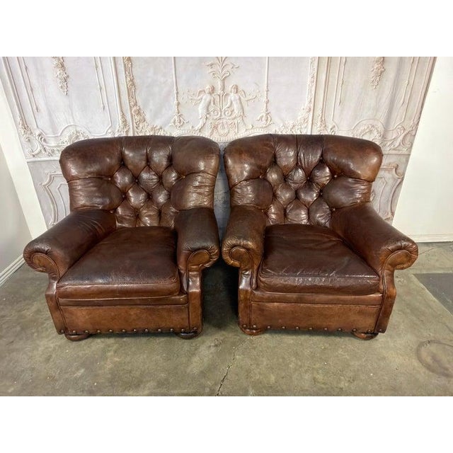 A commanding pair of oversized leather tufted club chairs that embody the timeless sophistication of a British gentlemen’s...