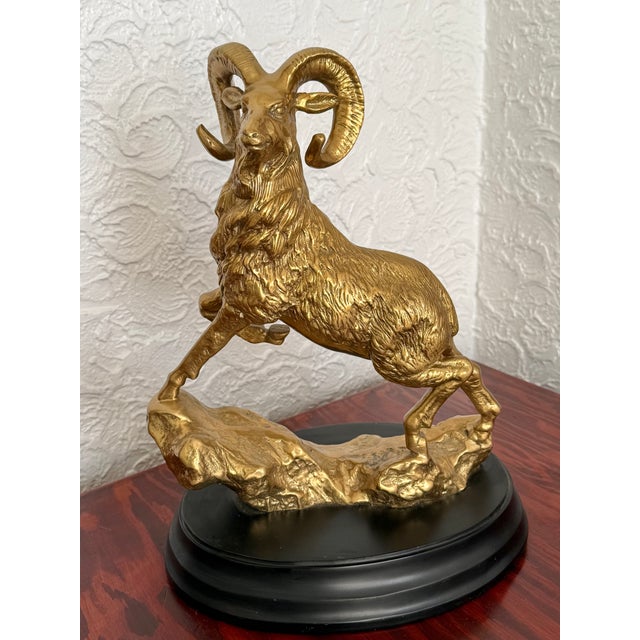 Cast solid brass ram statue, shown surveying from a rocky outcrop. The cast detail is rich, with deep textured fur and...
