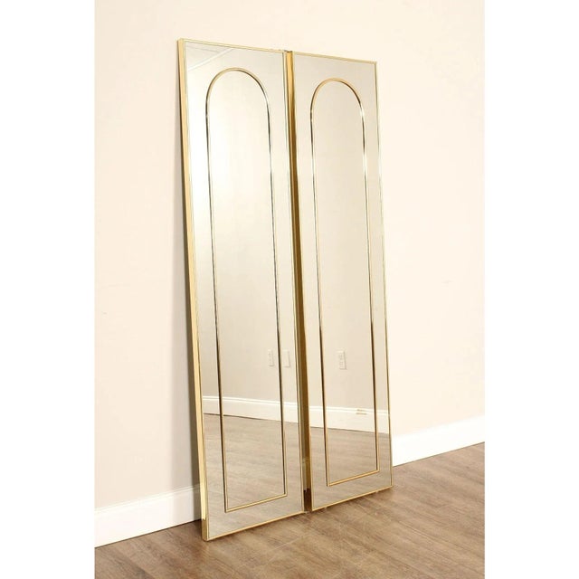 Bi-fold floor mirror with slim brass-tone frames and integrated arched detailing. Minimal architectural form with clean...