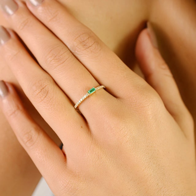 Refined and minimalist, this elegant band ring is crafted in 14k yellow gold and features a sleek 0.09 carat emerald-cut...