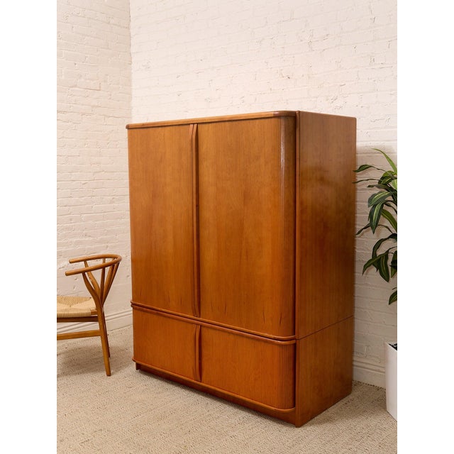 A handsome vintage Mid-Century Modern media cabinet featuring warm honey-toned wood, softly rounded corners, and tall...