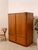 A handsome vintage Mid-Century Modern media cabinet featuring warm honey-toned wood, softly rounded corners, and tall...