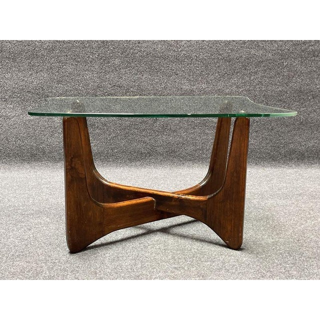 MCM accent table featuring a wood base and a clear glass top. The design includes intersecting wooden supports and a glass...