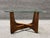 MCM accent table featuring a wood base and a clear glass top. The design includes intersecting wooden supports and a glass...