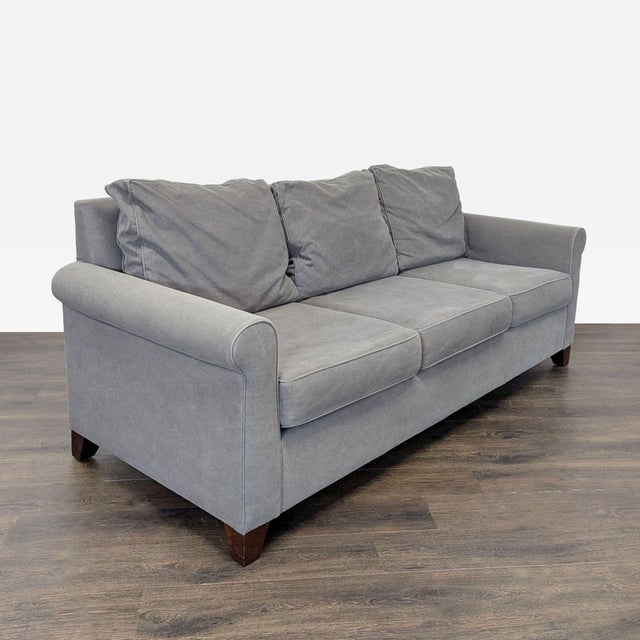 This Pottery Barn 3-seat sofa features a soft gray fabric and classic design with rolled arms and sturdy wooden legs....