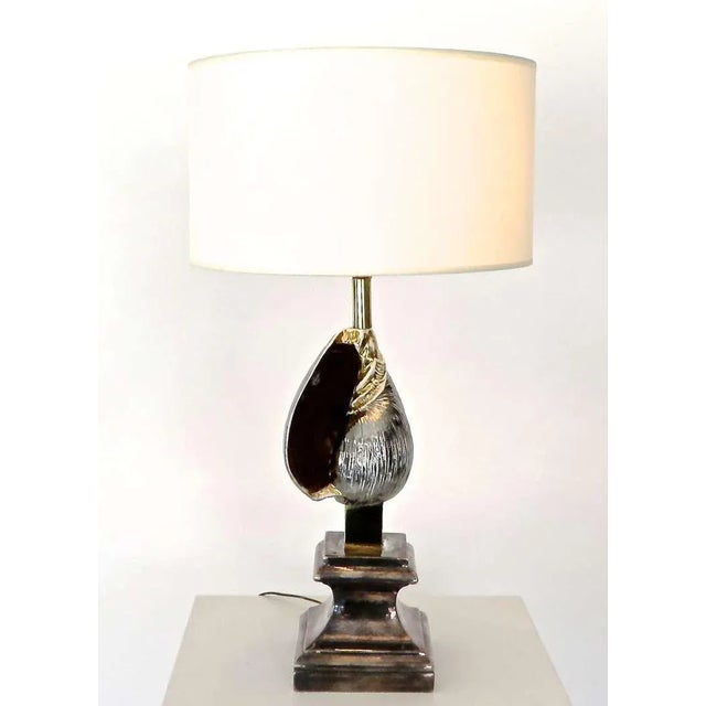 A French table tamp with silver and gold glazed accent ceramic seashell on a classical pediment. Brass accents between the...