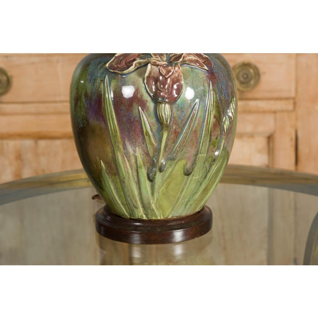 A green glazed 1920s pottery table lamp with raised floral motif, brown accents and circular wooden base. Evoke a sense of...