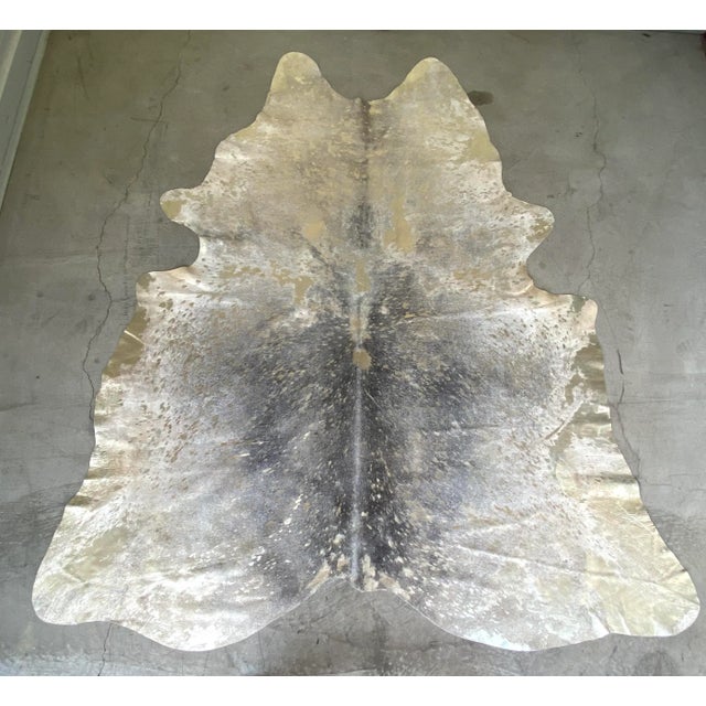 Stunning large natural Brazilian cowhide in variegated shades of gray with gold metallic spatters. The contrast against...
