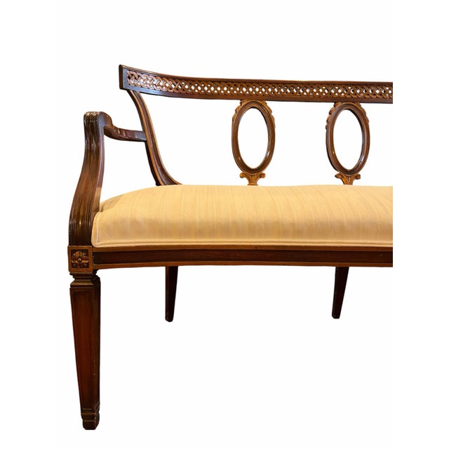 An antique mahogany settee with ornately by carved openwork patterned back and off-white striped upholstery.