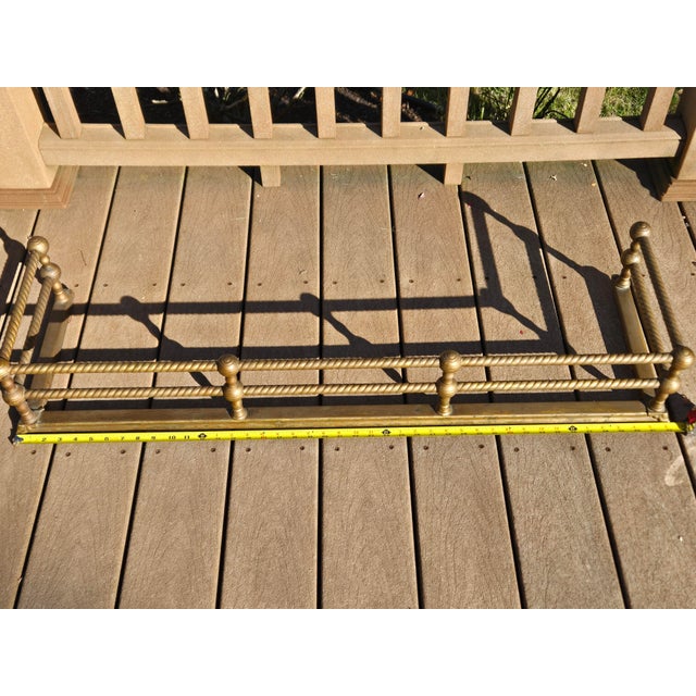 Antique brass fireplace fender with twisted rails and ball posts. Fair condition with wear and patina from age and use....