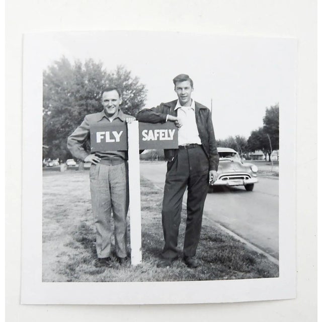 Circa 1950's snapshot photograph. 2 men standing by a sign reading Fly Safely. Unframed, 3.5" sq. good condition.