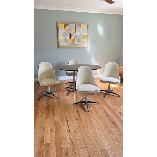 4 swivel chairs featuring ergonomic scoop silhouette, chrome atomic-style base and two-tone vinyl upholstery with cream...