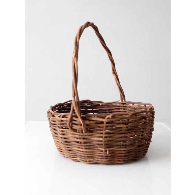 A vintage handwoven wicker basket with a rounded form and an easy arched handle, crafted in natural fibers with subtle...