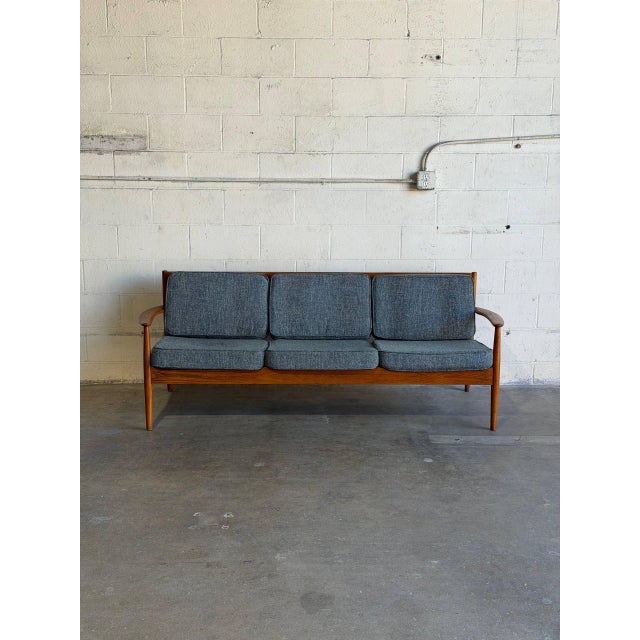 This Model 56 three-seater couch features an elegant open frame with softly curved armrests and an angled back profile....