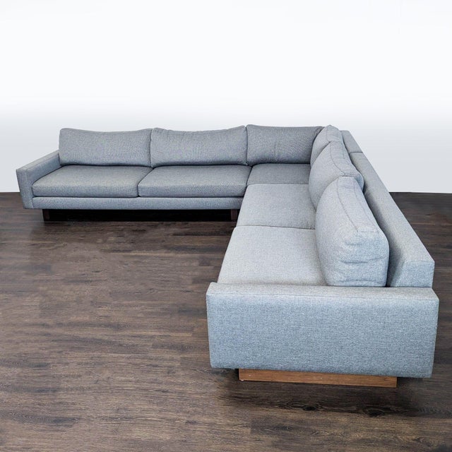 This Room & Board sectional features a clean, modern design with soft gray fabric and a sturdy wooden base. The L-shaped...