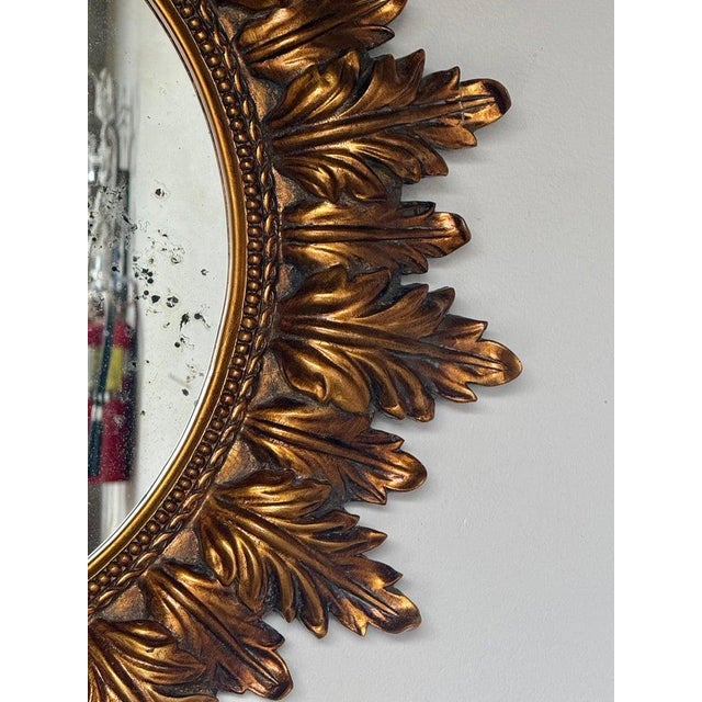 A striking mid-century giltwood sunburst mirror featuring a richly carved frame composed of radiating acanthus leaves...