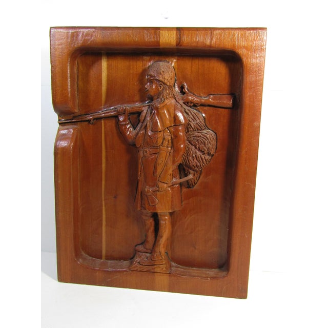 Intricately hand-carved wooden relief depicting a frontiersman carrying a rifle over his shoulder with a fur pelt strapped...