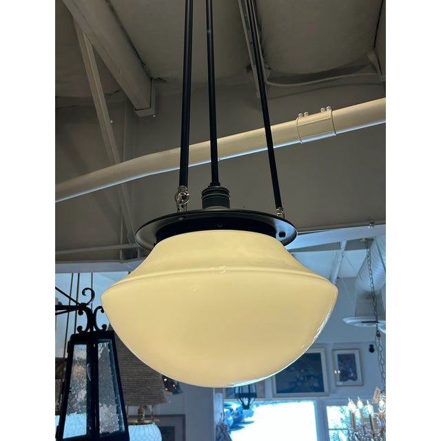Oil-rubbed bronze pendant with a round opal glass bowl shade. The shade is suspended from a circular ceiling canopy by...