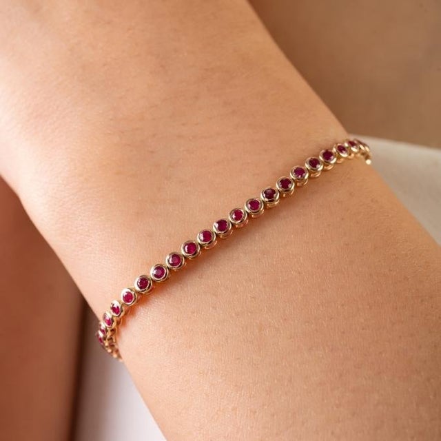 This elegant tennis bracelet features natural round-cut rubies totaling 1.65 carats, set in rich 14k yellow gold. The...