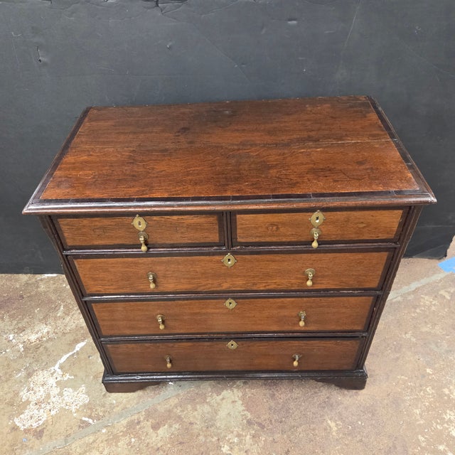 This Georgian 5 Drawer Oak Chest With Dark Cherry Banding With Brass Drop Pulls & Ecutcheons is set on bracket feet. It is...