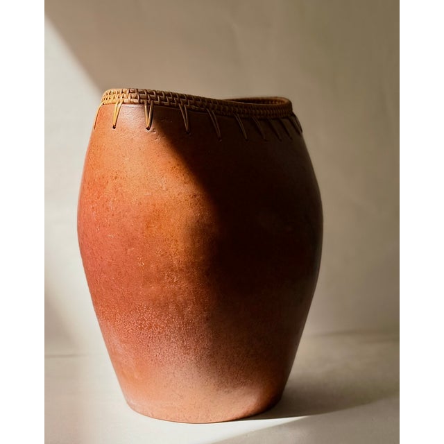 A sculptural pair of vintage Indonesian terracotta vessels featuring handwoven rattan rims and looped lacing. Each vessel...