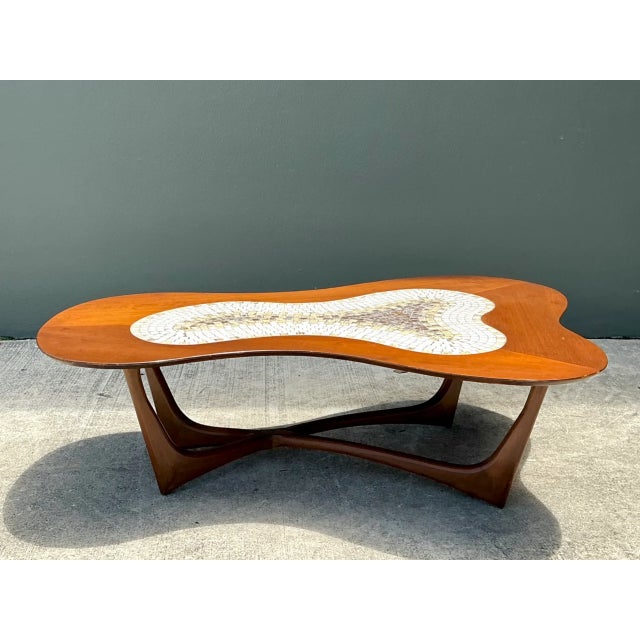 This vintage biomorphic coffee table pairs a sculptural wood base with an eye-catching ceramic mosaic top, embodying mid-...