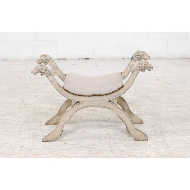 An Italian midcentury Empire style painted bench with carved ram heads and new upholstery. This exquisite Italian painted...