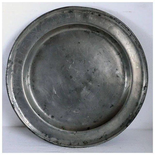 DETAILS A large antique, European pewter plate of round form with a wide rim and reeded edge. It is decorated with wriggle...
