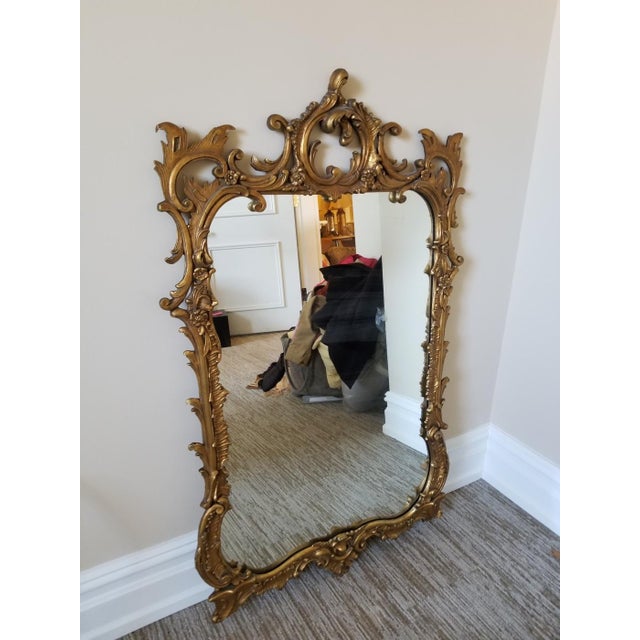 A large ornate gold-gilded French Rococò-style decorative carved framed mirror with scrolling foliage, floral accents, and...
