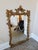 A large ornate gold-gilded French Rococò-style decorative carved framed mirror with scrolling foliage, floral accents, and...