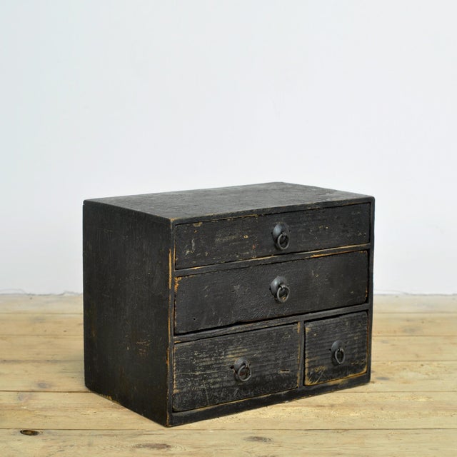 An atmospheric small Japanese tansu—specifically a compact ko-dansu—featuring four drawers. The chest is fitted with...